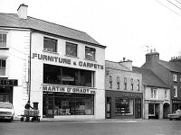 Shop St, Westport, July 1972. - Lyons0014748.jpg  Shop St, Westport, July 1972. Left to right : Doherty's Chemist, Martin O' Grady's, the Cake Kitchen (proprietors Colm Feeny and Mary Gill Feeny), O' Donnells and Molloys' Hardware. : 19720727 Shop St 2.tif, Lyons collection, Westport